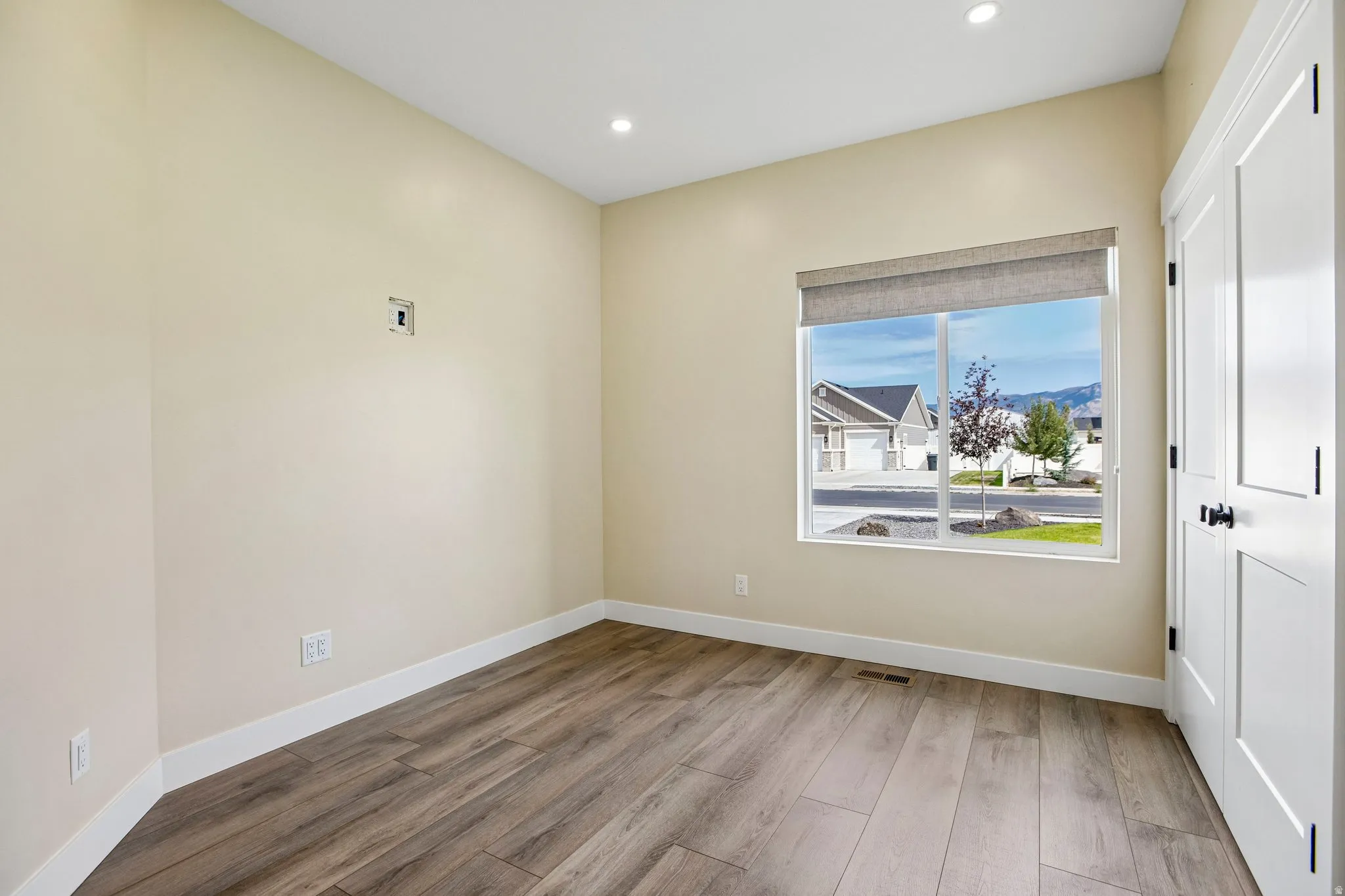 Recessed lighting, wood-finish flooring, white trim, and a window with a roller shade