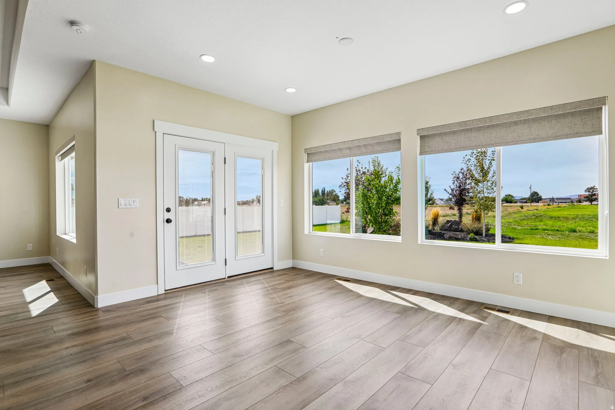 Wood-finish plank flooring, recessed ceiling lighting, dual pane windows with roller shades, and white frame French doors