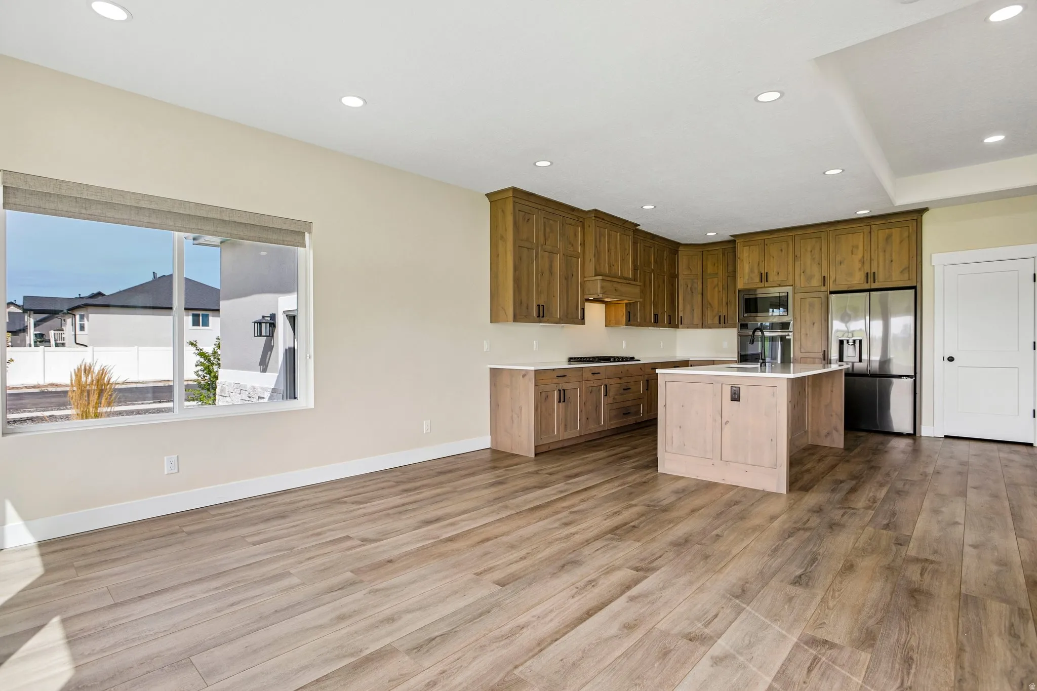 Open-concept kitchen and living area featuring wood-finish flooring, recessed lighting, and a large window