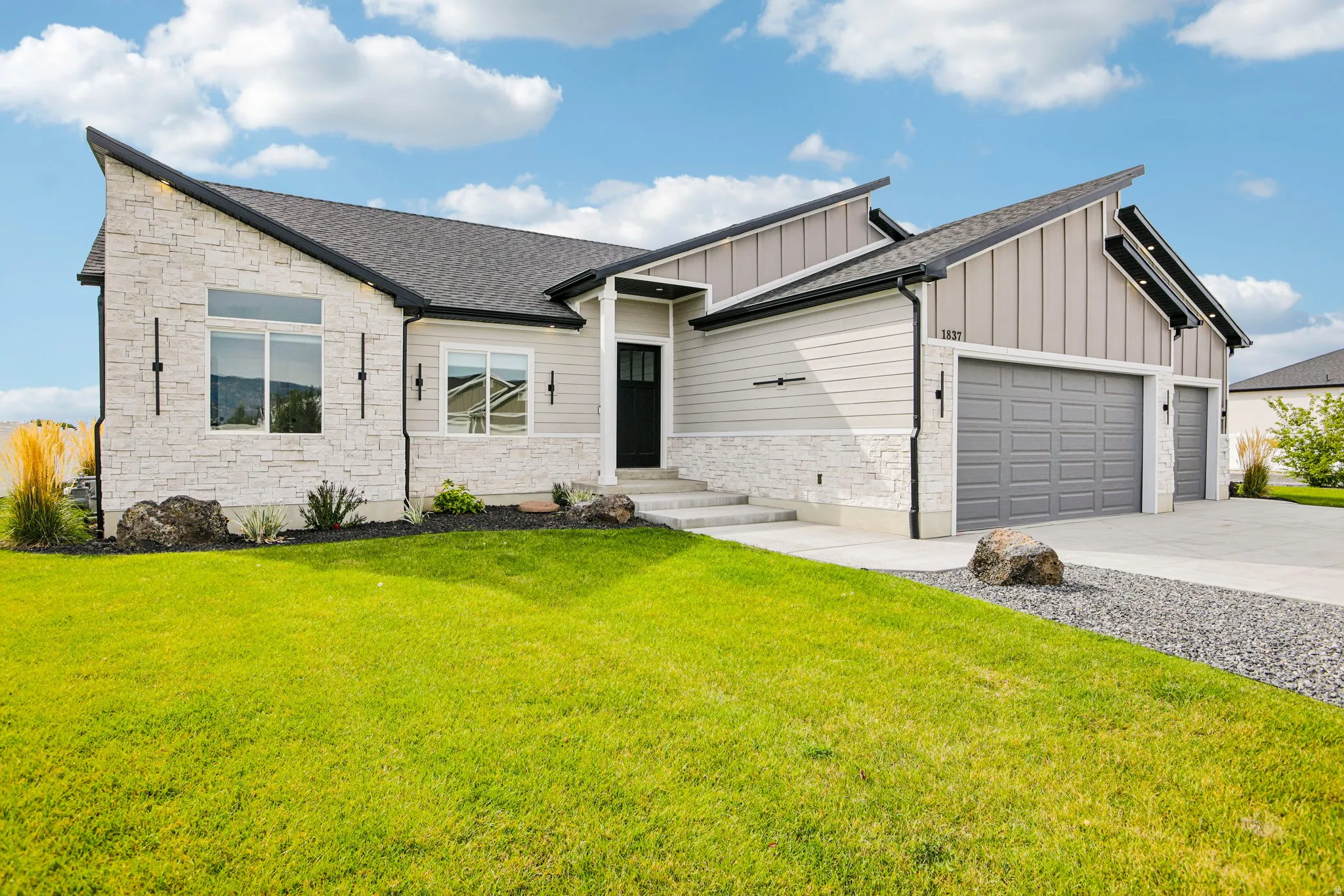 Modern exterior with a stone and siding facade, multi-pitch roofline, attached multi-car garage, and concrete driveway