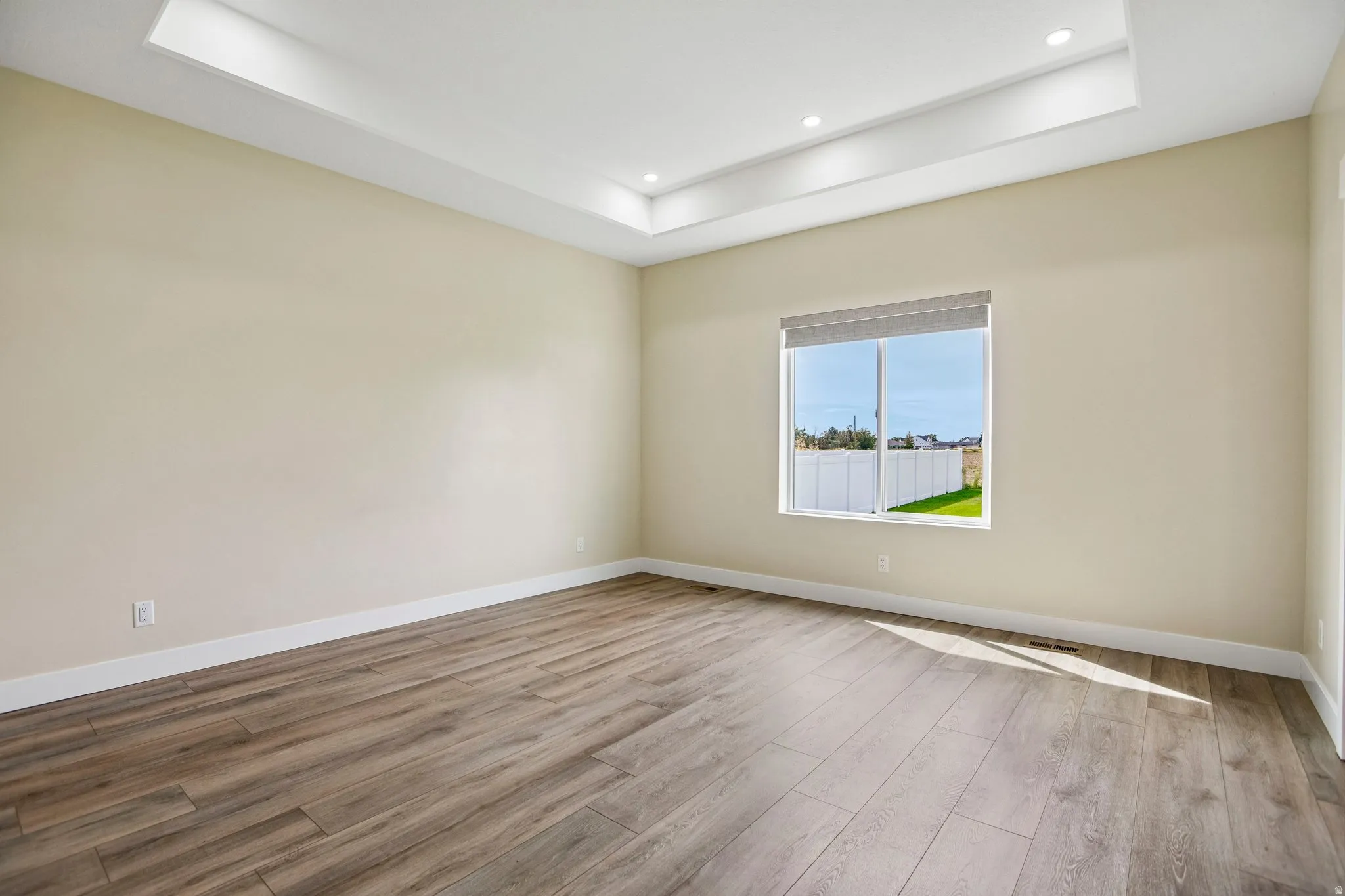 Recessed lighting illuminating a tray ceiling, wood-finish flooring, and a large window