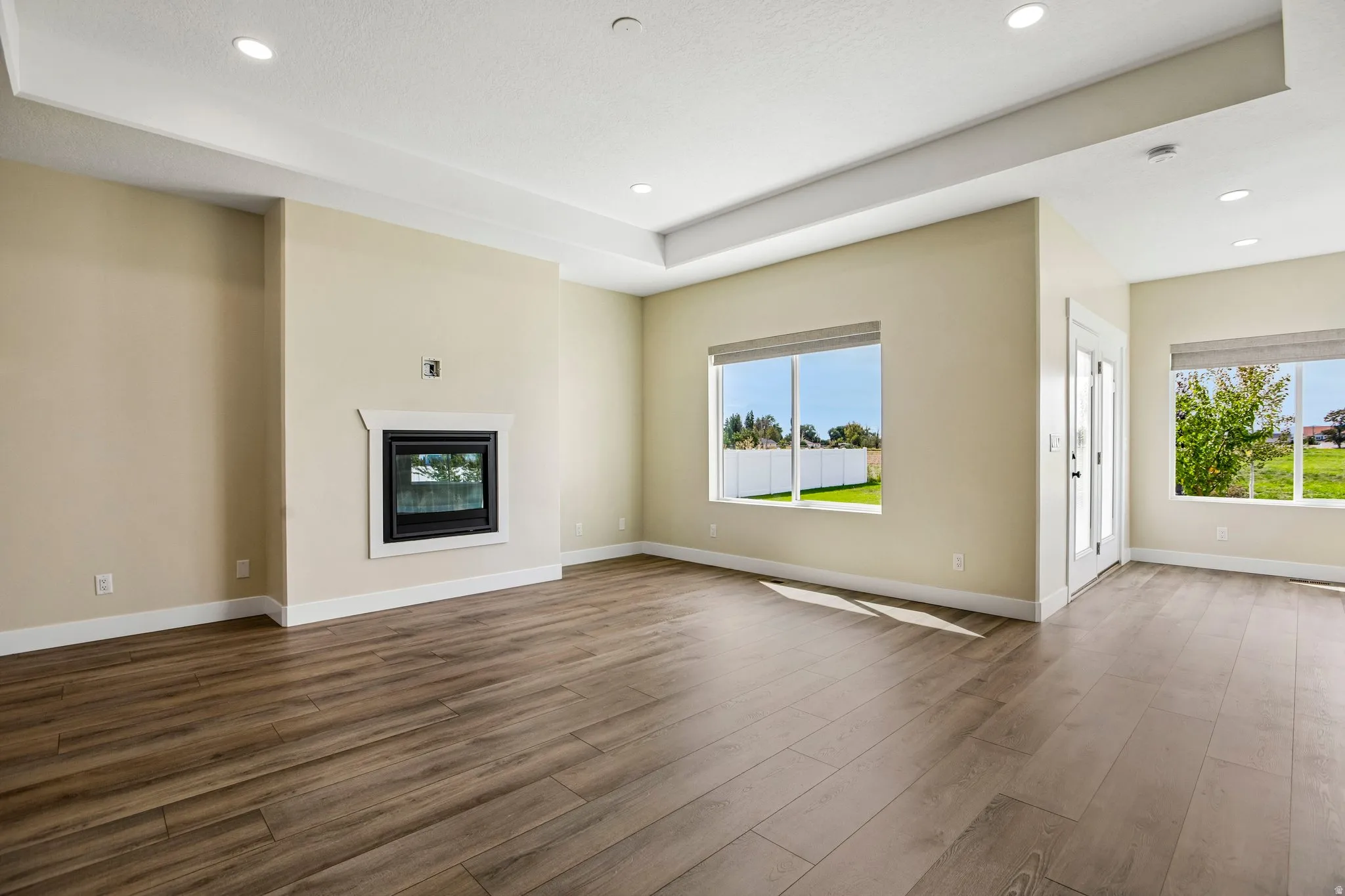 Spacious living area featuring wood-finish flooring, a fireplace with a white mantel, and a tray ceiling