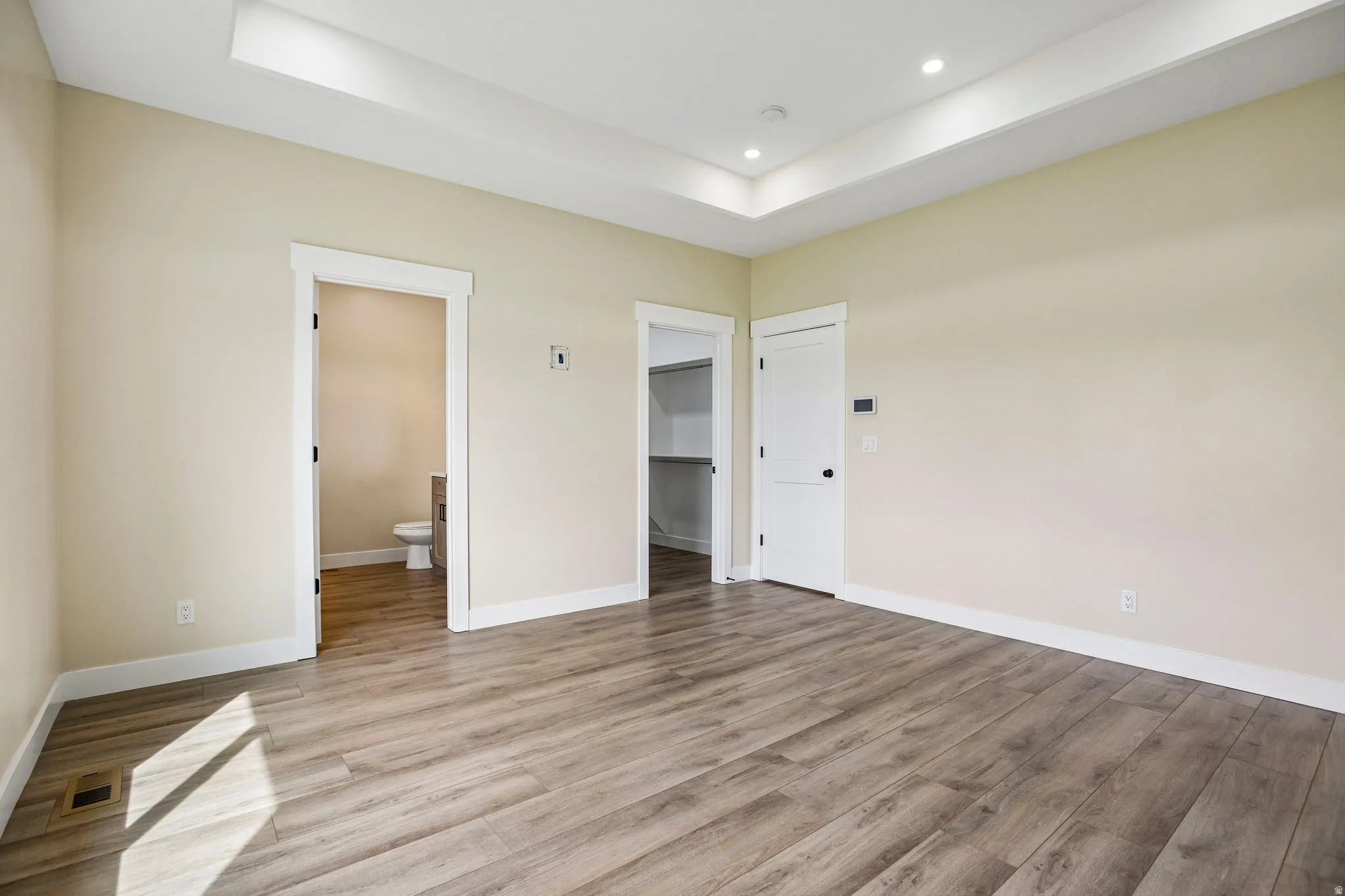 Recessed lighting, tray ceiling, wood-finish flooring, white trim, and a built-in closet