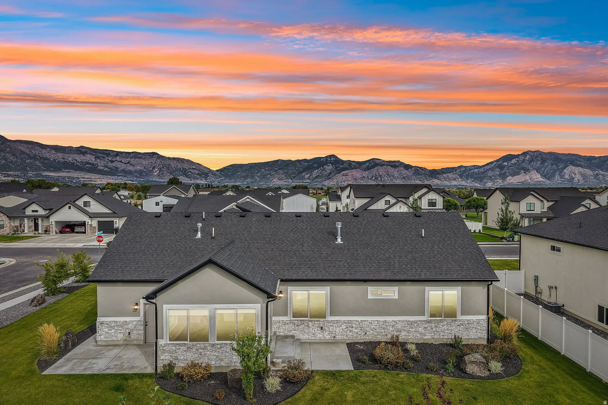 Stucco exterior with stone accenting, dark shingle roof, established landscaping, manicured lawn, and mountain scenery