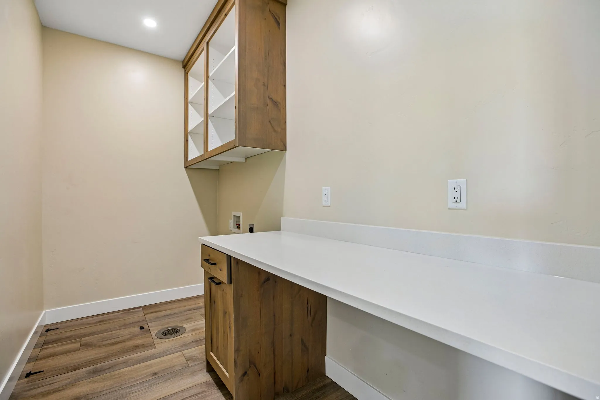 Wood-finish flooring, recessed lighting, wood cabinetry with glass-front uppers, and a white countertop