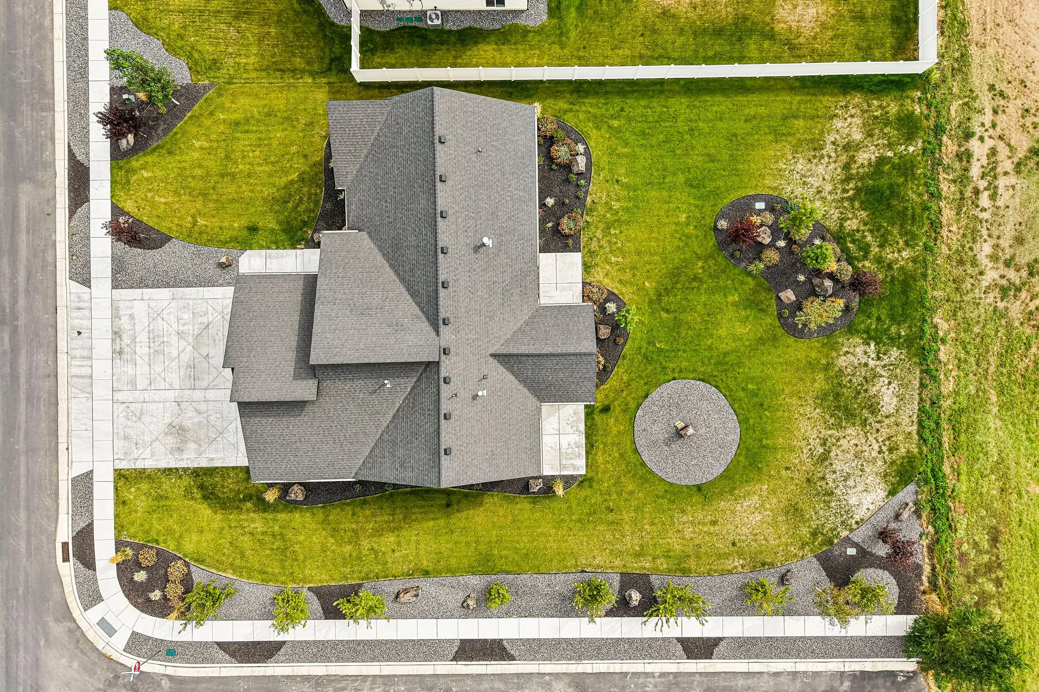 Asphalt shingle roof, concrete driveway with decorative etching, gravel landscaping beds, concrete sidewalks, and a manicured lawn