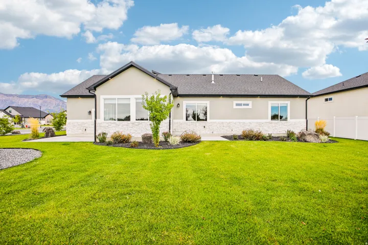 Stucco and stone exterior, dark shingle roof, established landscaping, white vinyl privacy fencing, and mountain backdrop