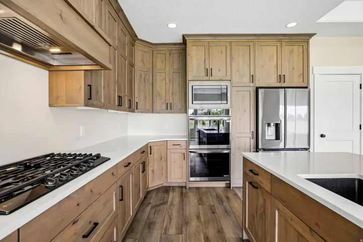 Light wood-finish cabinetry with black hardware, white countertops, built-in stainless steel appliances, and wood-finish flooring