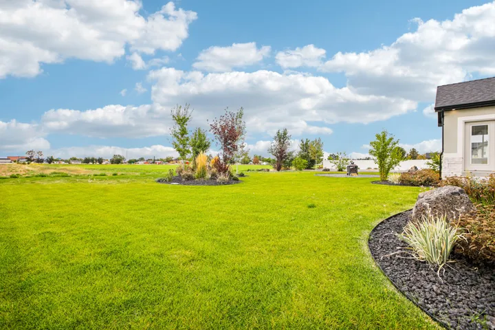 Expansive green lawn with established landscaping beds, decorative rock, and mature plantings