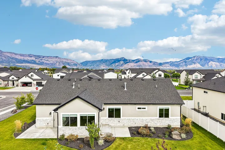 Exterior featuring a dark shingle roof, light stucco siding, stone accents, and multiple windows