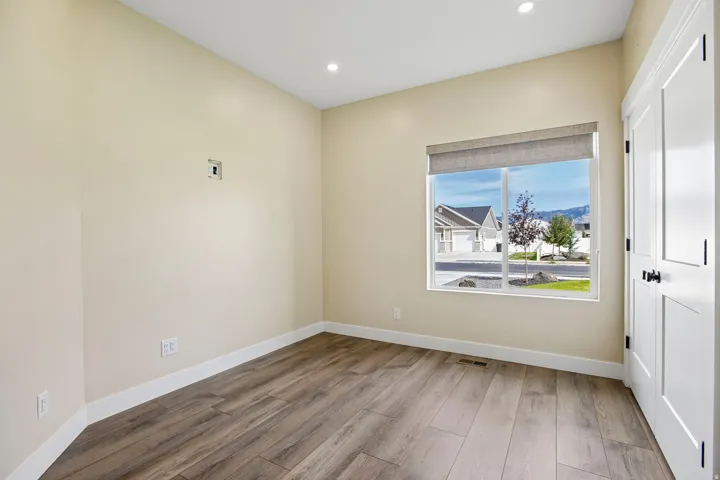 Recessed lighting, wood-finish flooring, white trim, and a window with a roller shade