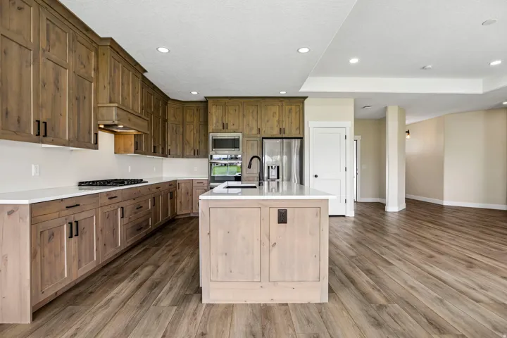 Kitchen featuring wood-finish cabinetry, stainless steel appliances, a center island with sink, white countertops, and wood-finish flooring