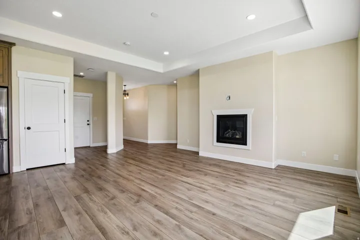 Hardwood-finish flooring throughout, featuring a built-in fireplace with a white mantel, recessed lighting, and a tray ceiling