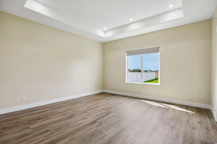 Recessed lighting illuminating a tray ceiling, wood-finish flooring, and a large window