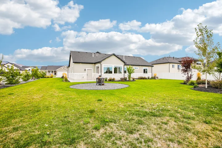 Expansive backyard featuring a manicured lawn, landscaping with mature plantings, and a gravel patio with a fire pit