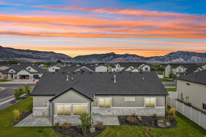 Stucco exterior with stone accenting, dark shingle roof, established landscaping, manicured lawn, and mountain scenery
