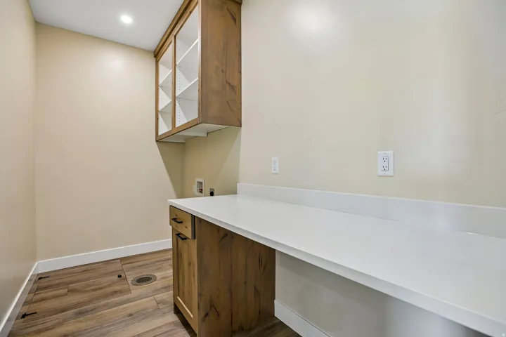Wood-finish flooring, recessed lighting, wood cabinetry with glass-front uppers, and a white countertop