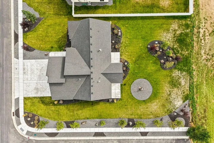 Asphalt shingle roof, concrete driveway with decorative etching, gravel landscaping beds, concrete sidewalks, and a manicured lawn