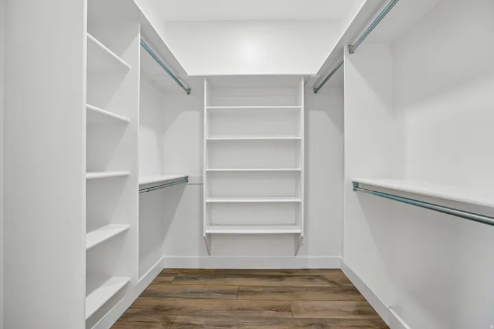 Walk-in closet with extensive built-in shelving, multiple hanging rods, and wood-finish flooring