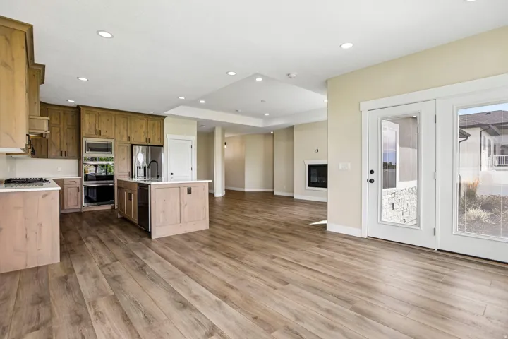 Wood-finish flooring throughout, kitchen with wood cabinetry and stainless steel appliances, central kitchen island with sink, recessed lighting, and double glass-paneled doors