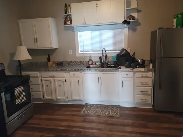 White cabinetry with brushed nickel hardware, speckled countertops, wood-finish flooring, and a stainless steel refrigerator