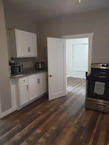 Wood-finish flooring, white flat-panel cabinetry, granite-style countertop, stainless steel range, and white interior door