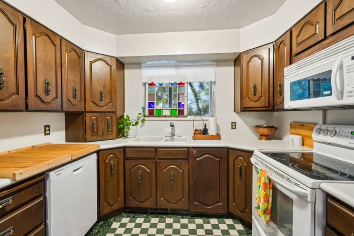 Kitchen featuring wood cabinetry, white countertops, built-in dishwasher, and a double basin sink