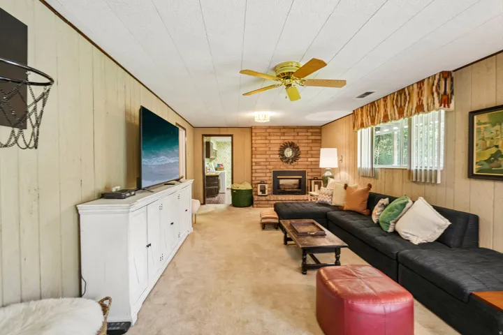Recessed fireplace with brick surround, ceiling fan, carpeted flooring, and paneled walls