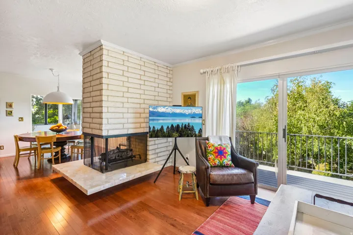 Hardwood flooring, brick fireplace with a stone hearth, sliding glass door, and balcony with metal railings