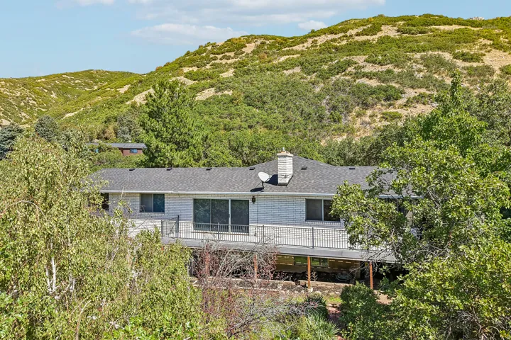 White brick exterior, dark shingle roof, sliding glass doors, exterior deck with dark railing, prominent chimney