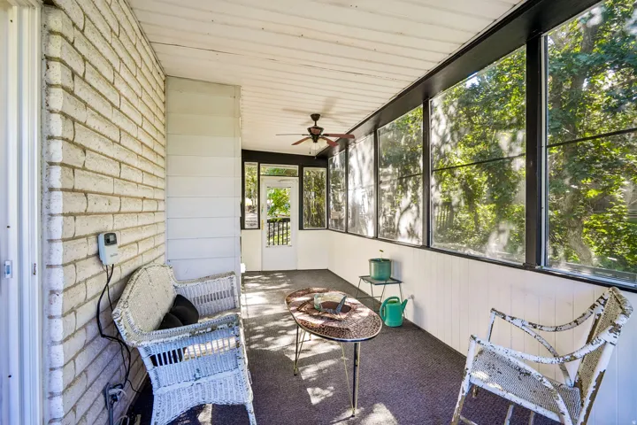 Screened porch featuring a white brick wall, wood paneling, black window frames, and a ceiling fan