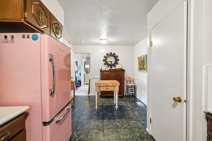 Wood-finish upper cabinetry, a vintage-style pink refrigerator, dark patterned flooring, and a white interior door with brass hardware