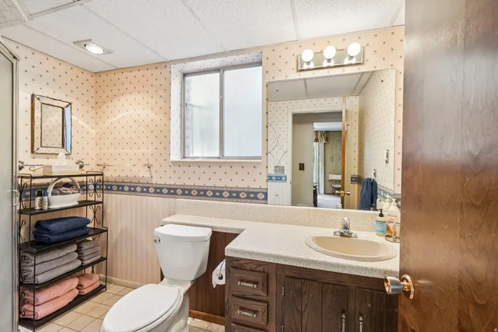 Bathroom featuring a single vanity with a countertop sink, wood cabinetry, a large wall-mounted mirror, and a frosted window