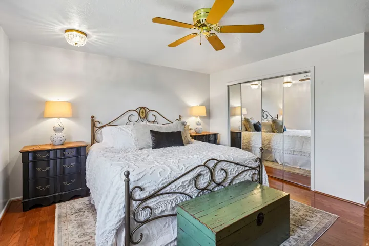 Wood-finish flooring, mirrored closet doors, and a ceiling fan