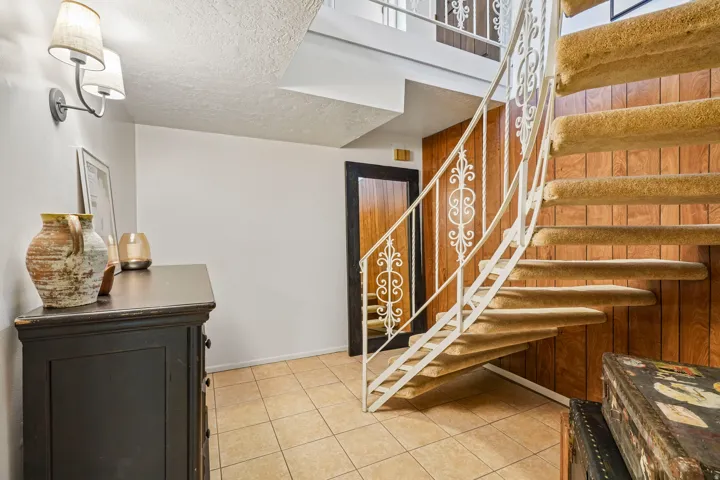 Curved staircase with carpeted treads and an ornate metal railing, complemented by wood paneling and tile flooring