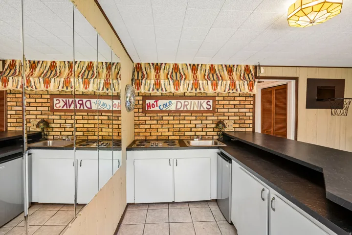 Compact kitchenette featuring a built-in electric stovetop, integrated sink, white cabinetry, and a textured brick-patterned wall