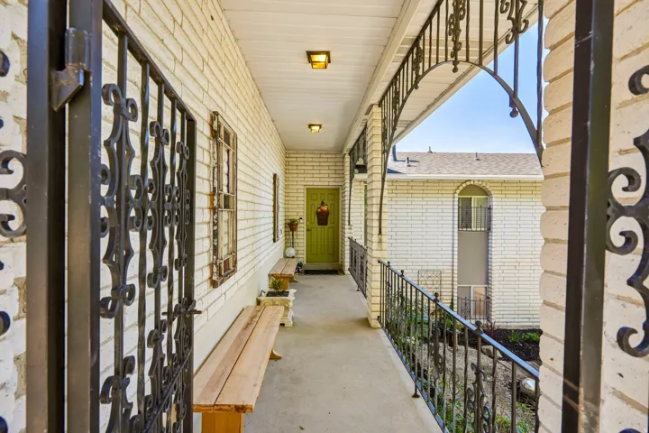 Covered entry with wrought iron railing and white brick exterior
