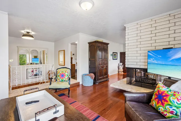 Hardwood flooring, white painted brick fireplace, light-toned fireplace hearth, white wall finishes, and white railing with decorative scrollwork