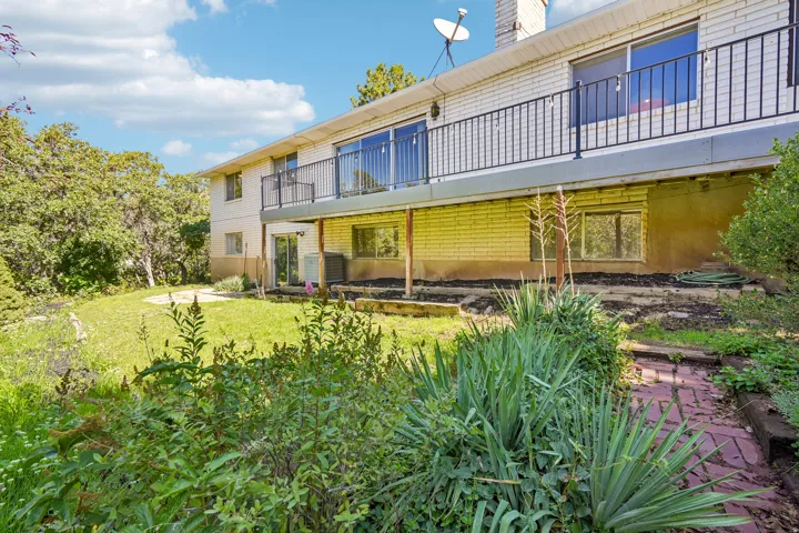 Multi-level exterior with a second-story balcony featuring black metal railing, lower level patio access, and a well-maintained lawn