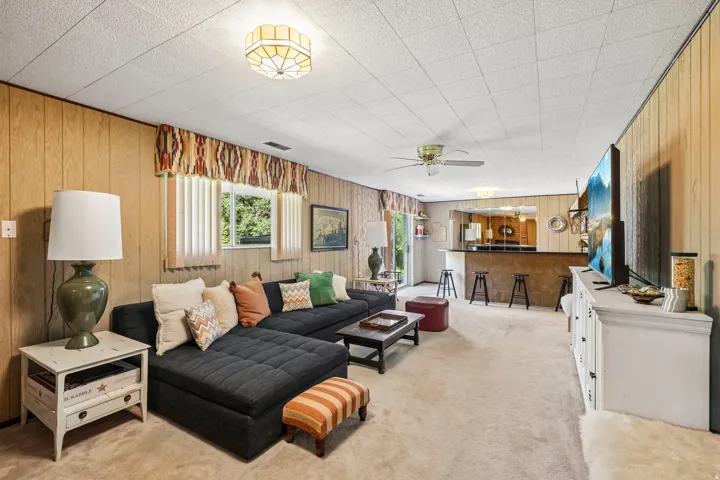 Recessed bar area with seating, wood paneling, acoustic tile ceiling, and ceiling fan