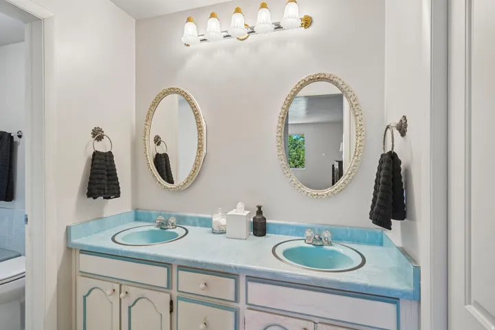 Dual oval mirrors, dual under-mount sinks, light blue countertop, and a vanity with cabinet storage