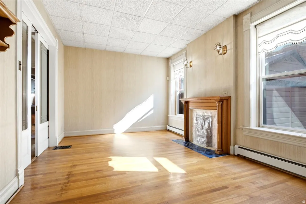 Hardwood flooring, decorative fireplace with tiled hearth, dual windows with molding, wall sconces, and double paneled doors