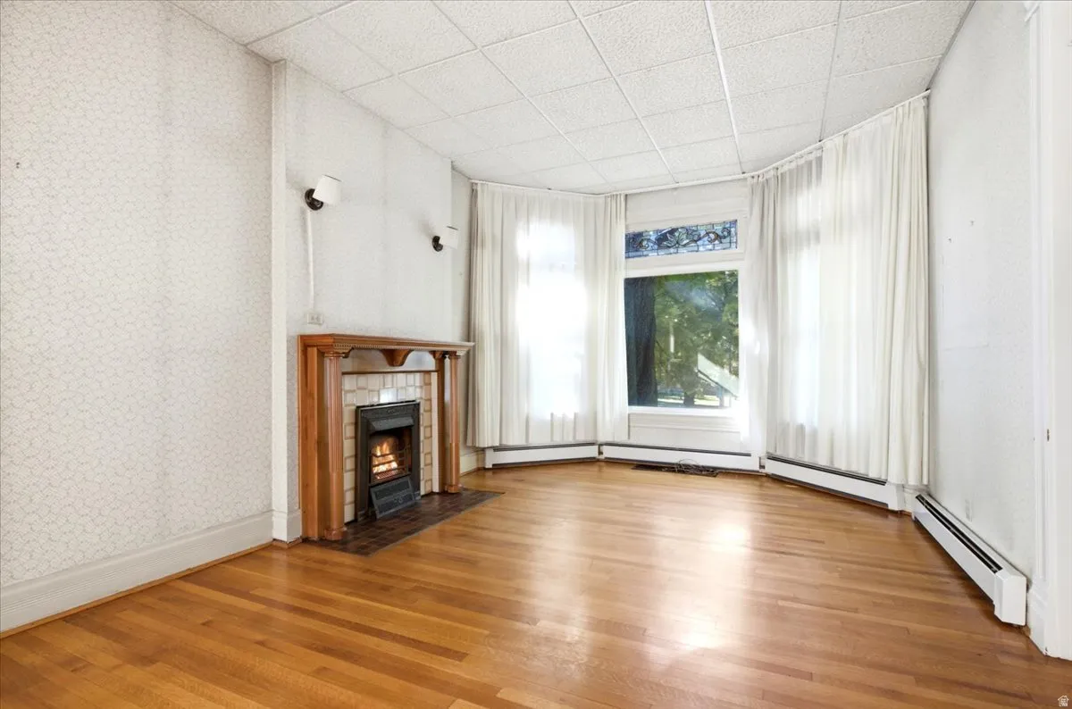 Hardwood flooring, fireplace with wood mantel, tiled hearth, built-in wall sconces, and multi-pane bay window