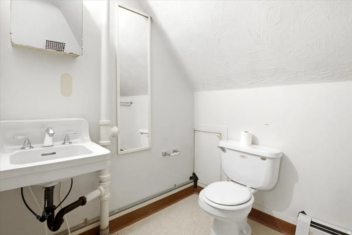 Pedestal sink with chrome faucet, wall-mounted mirror, white toilet, and textured ceiling finish