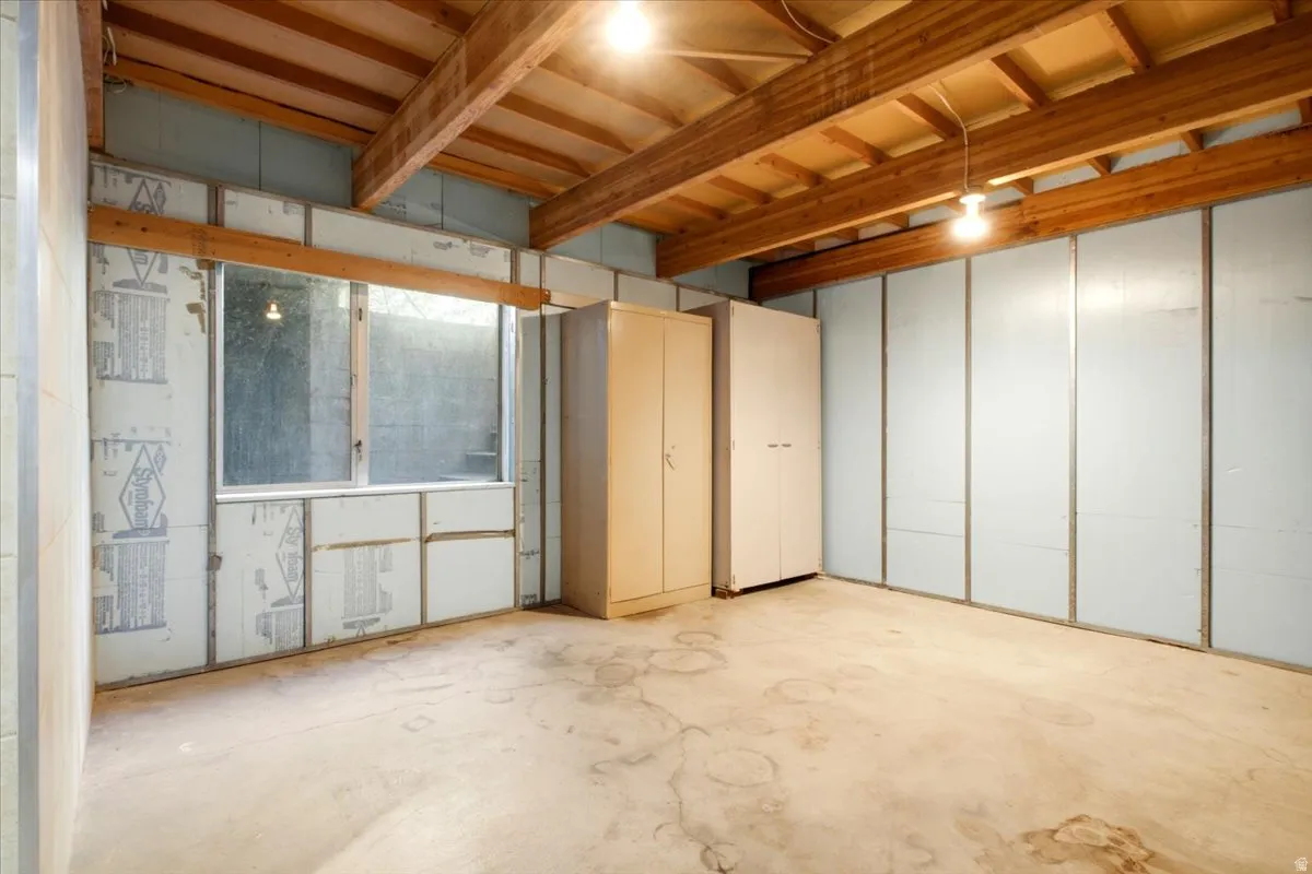 Exposed wood beam ceiling, concrete flooring, and an above-grade window