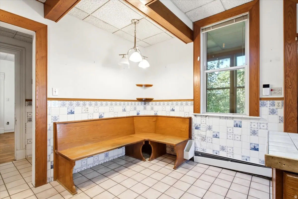 kitchen Built-in wood-finish banquette seating, tiled flooring, wood trim, drop ceiling, and a window