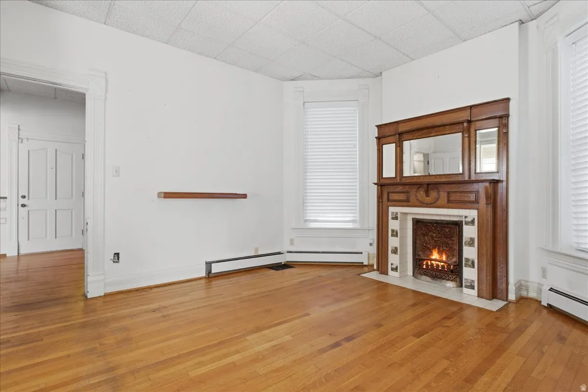 sitting room parlor Wood flooring, decorative fireplace with mantel, built-in mirror, and window treatments