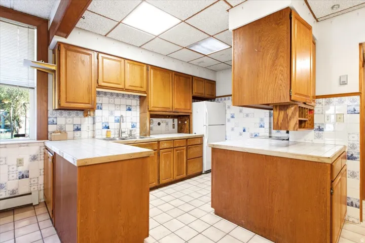 Wood cabinetry, tiled countertops, tiled flooring, tiled backsplash, and a stainless steel sink