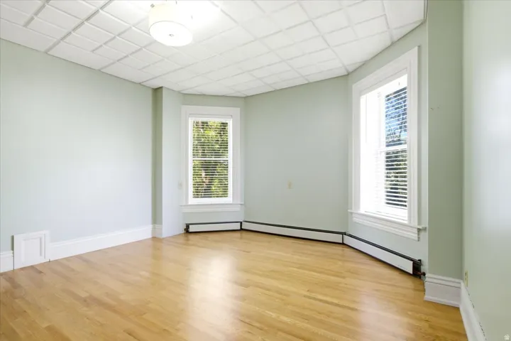 Southwest bedroom Hardwood flooring, two windows with blinds, baseboard heating, recessed ceiling, and a flush mount light fixture