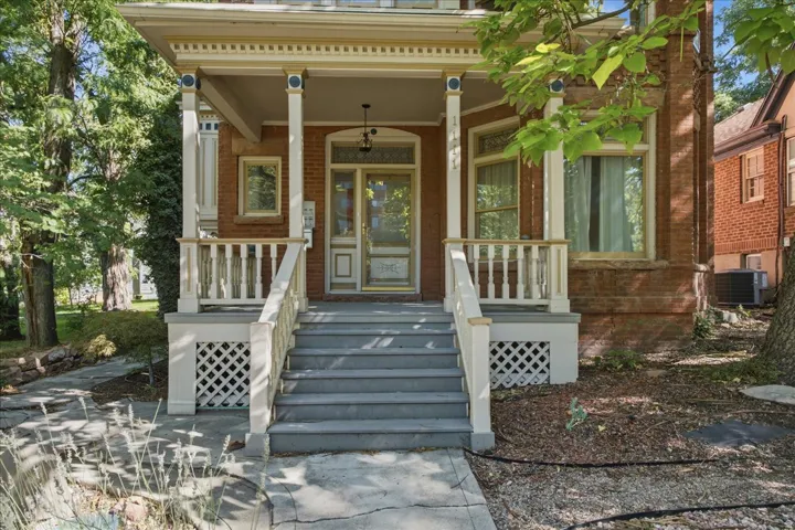 Brick exterior with a covered porch, white balustrade, detailed trim, and a prominent front entry